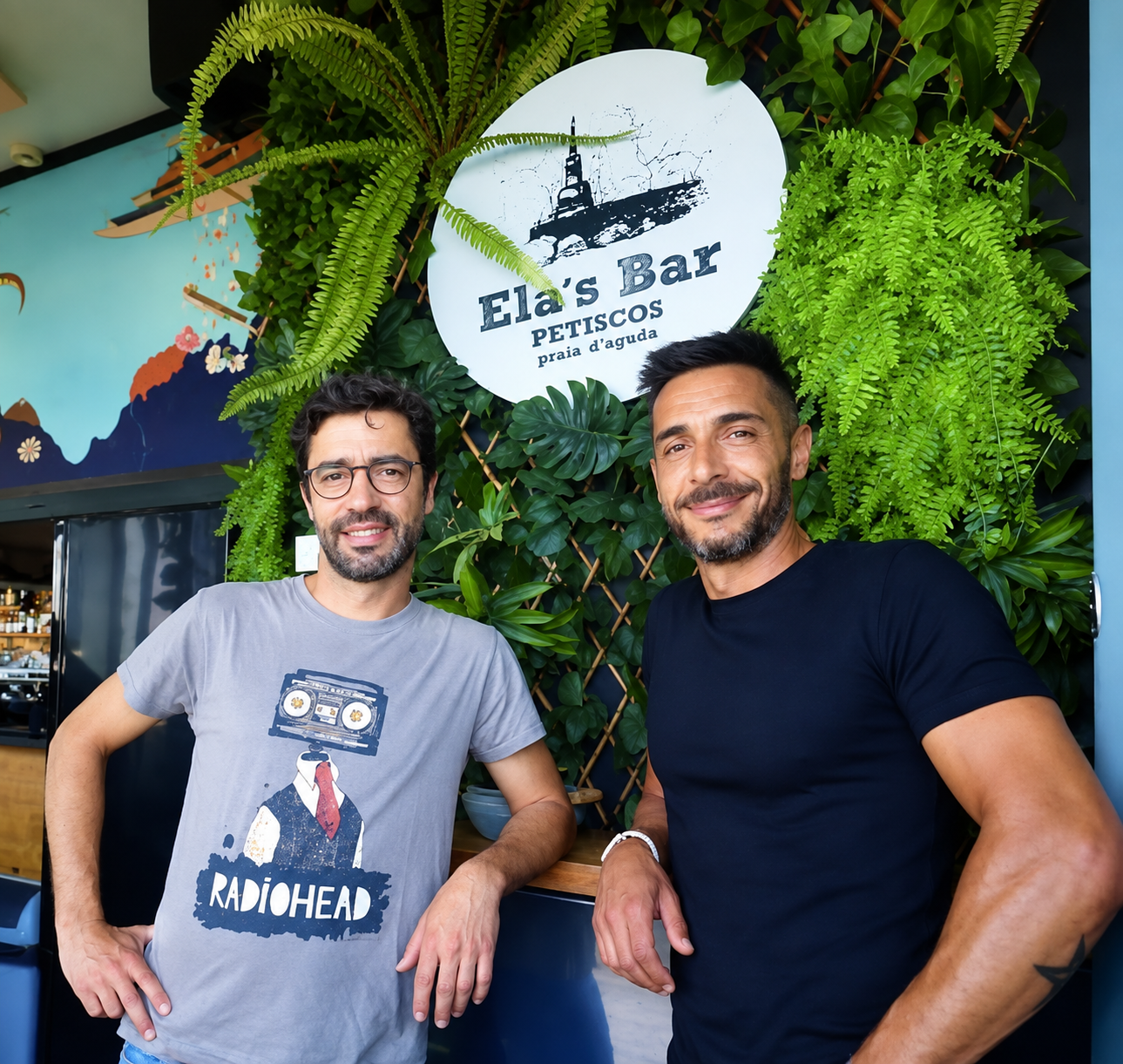 Dois clientes do Ela's Petiscos Bar junto à parede verde com o letreiro do bar